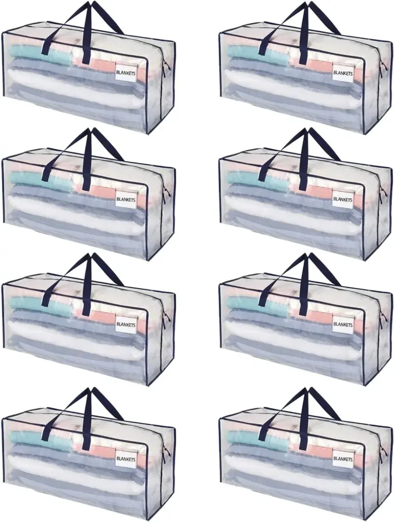 আটটি বড় স্বচ্ছ পোশাক স্টোরেজ ব্যাগ, each labeled "BLANKETS" এবং ভাঁজ কম্বল দিয়ে পূর্ণ, দৃ ur ় কালো হ্যান্ডলগুলি বৈশিষ্ট্যযুক্ত.